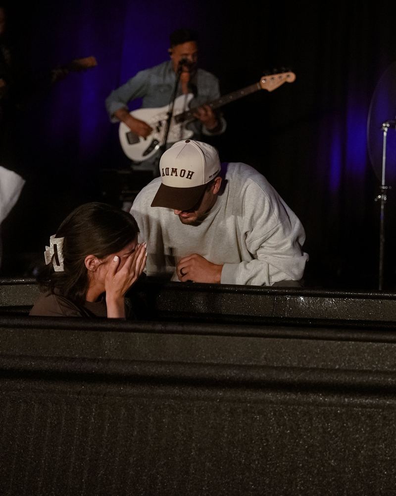 A woman in the tank covering her face in tears while a man in a ball cap leans in beside her