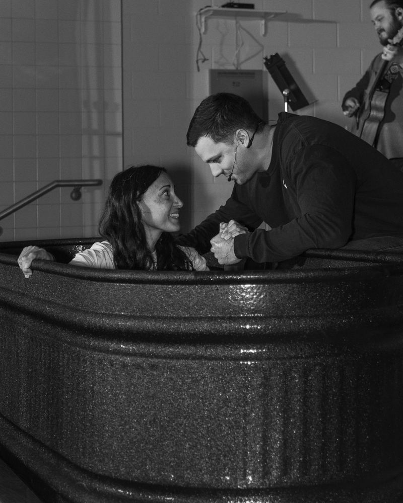 A woman in the tank looking up and smiling as the pastor grips her hand