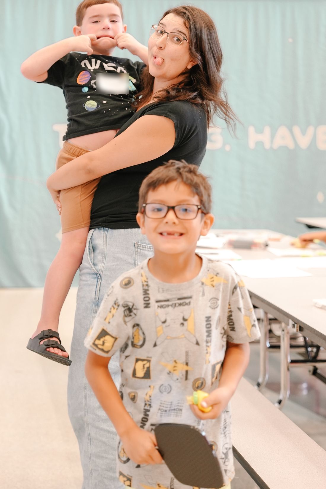 A volunteer holding a boy while they both make silly faces, with another boy grinning in front