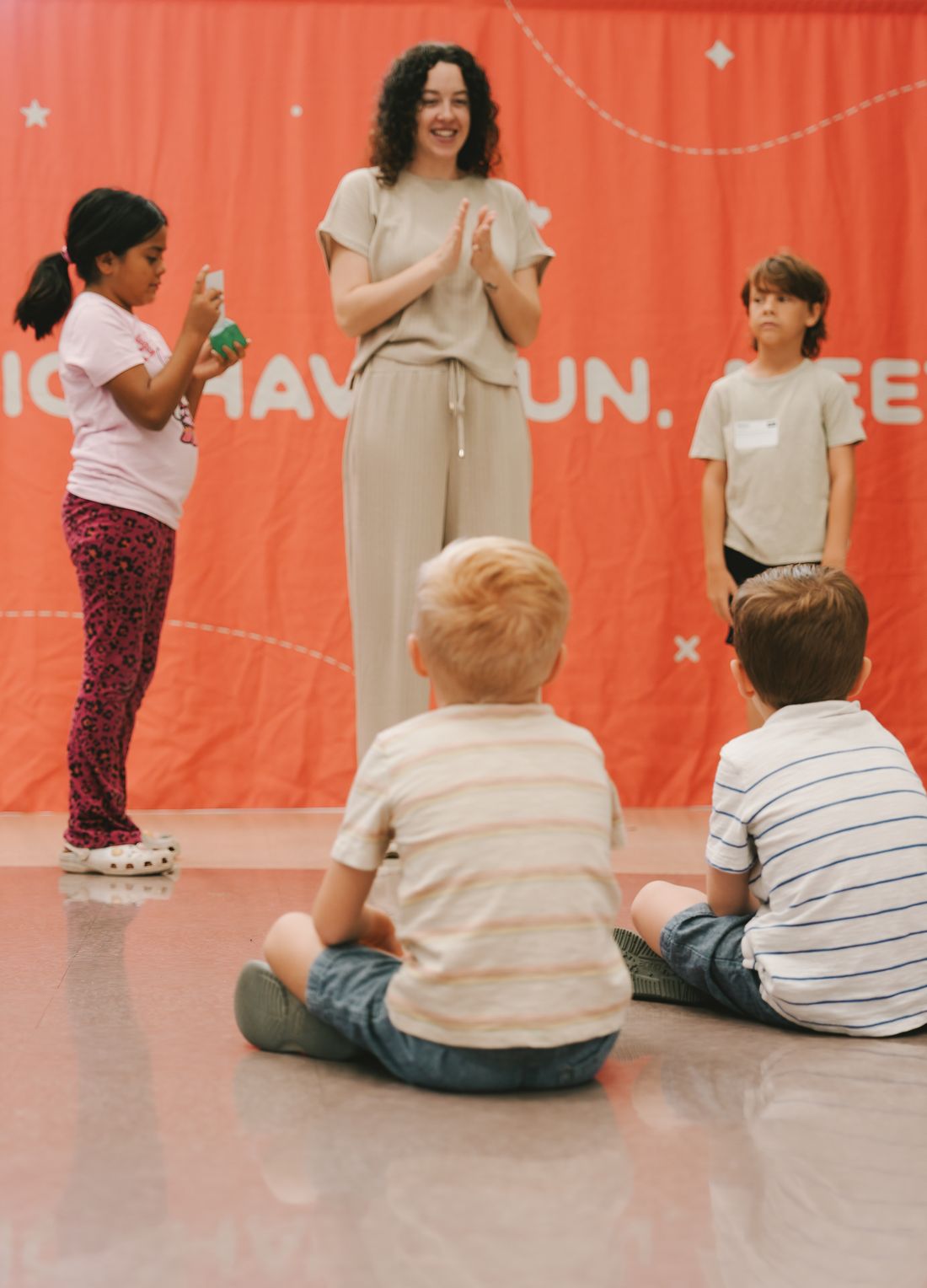 A leader clapping with a group of elementary kids in front of the Axiom Kids banner