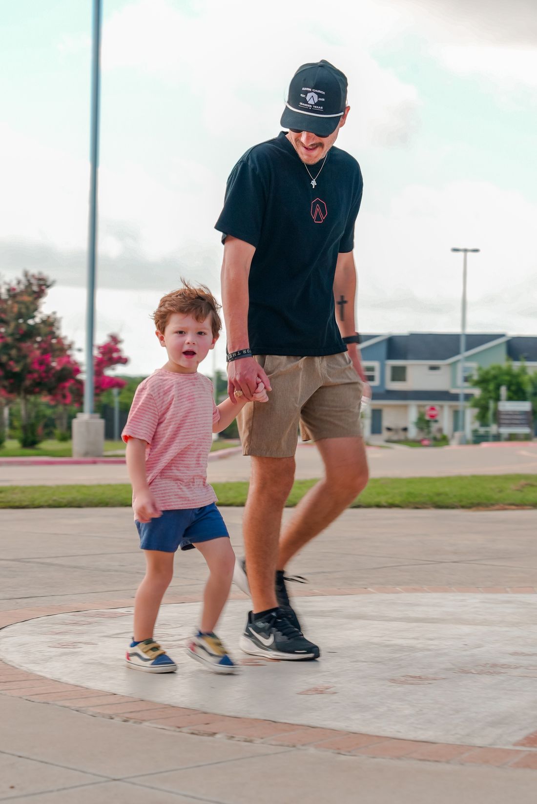 A dad in an Axiom Church hat walking in from the parking lot, holding his young son's hand