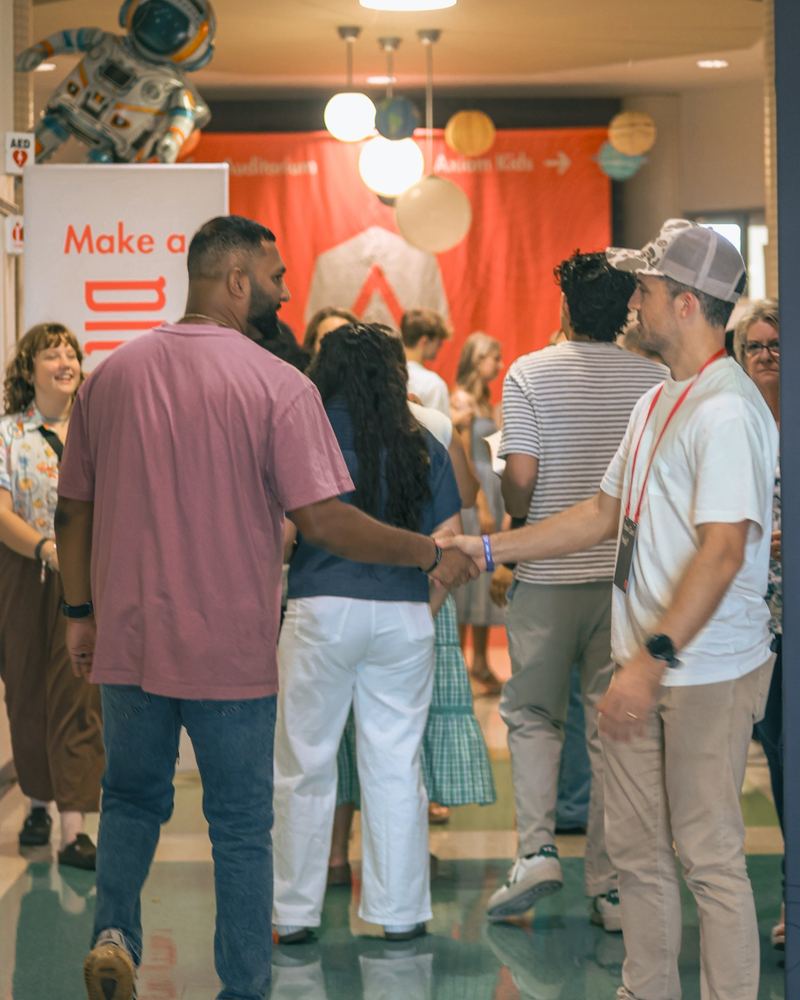 A volunteer shaking a man’s hand as people walk in