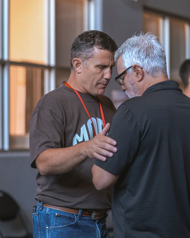 A volunteer praying with a man, hand on his shoulder