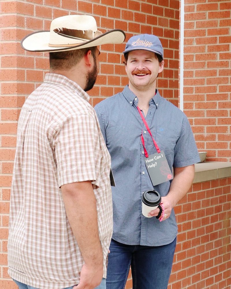Two men laughing together outside, one holding a coffee