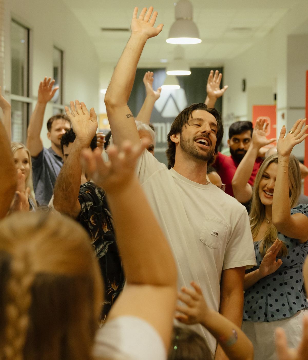 A crowd in the lobby with their hands in the air, a man in the middle laughing with his arm raised