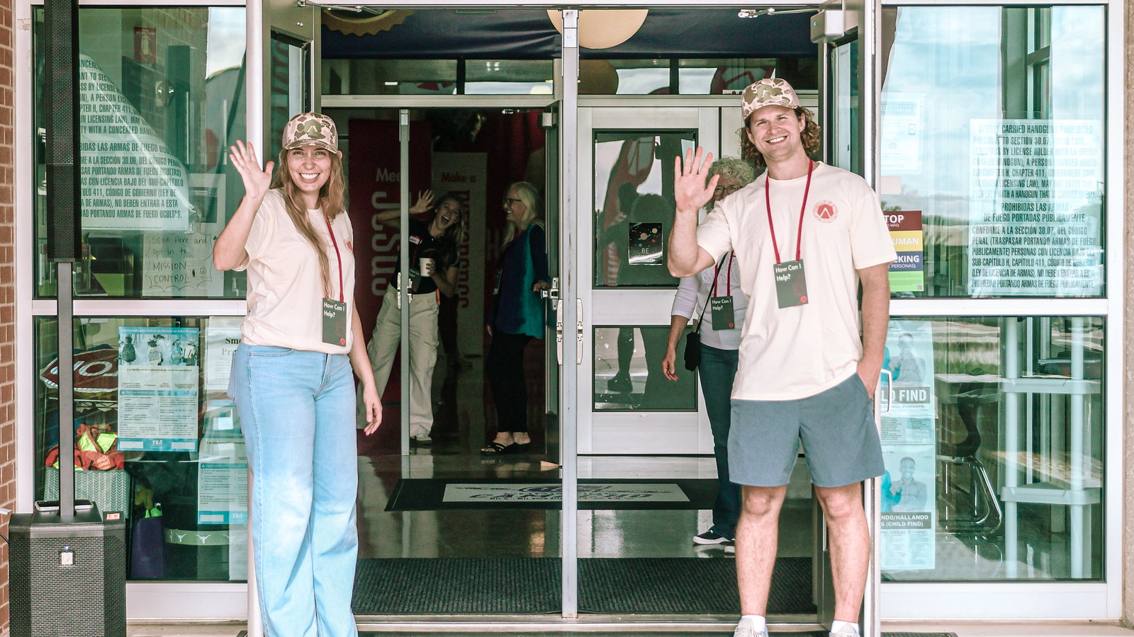 Two greeters waving from the front doors at Camacho Elementary