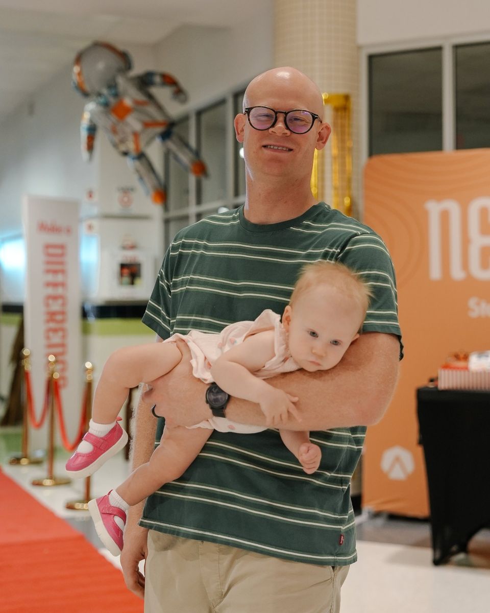 A dad smiling in the lobby with his baby daughter tucked under one arm