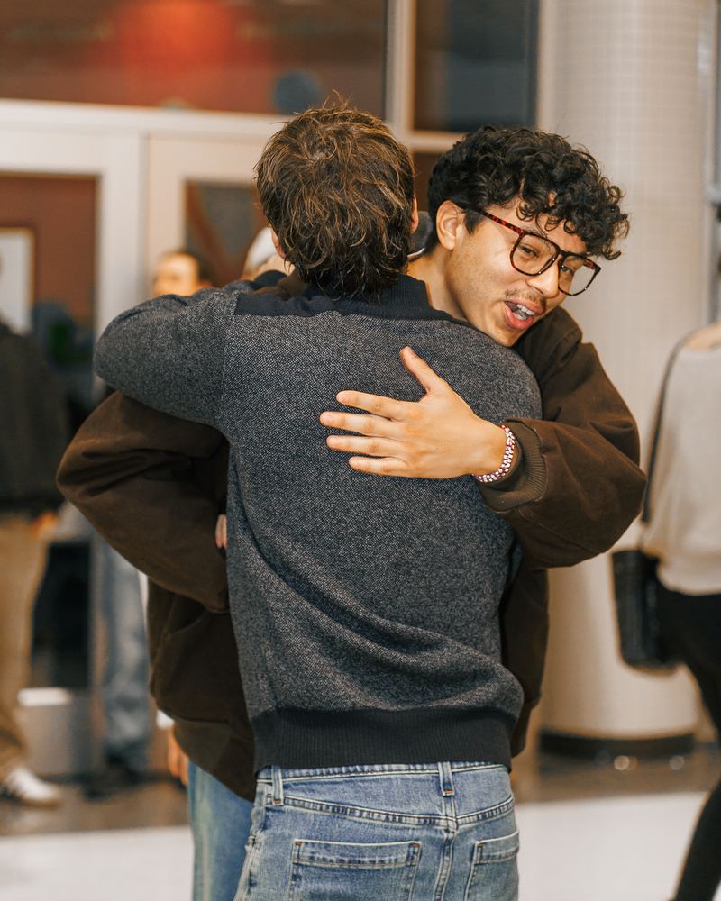 Two guys hugging in the lobby, one with his arm wrapped around the other's back