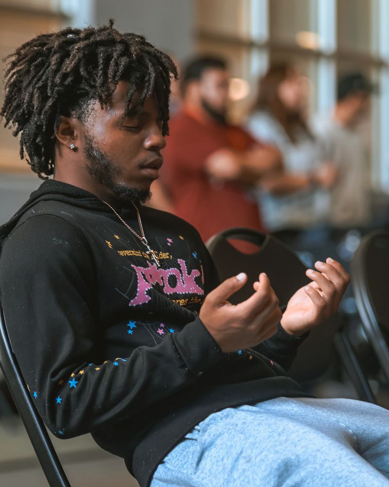 A young man sitting with his eyes closed and his hands open in front of him, praying