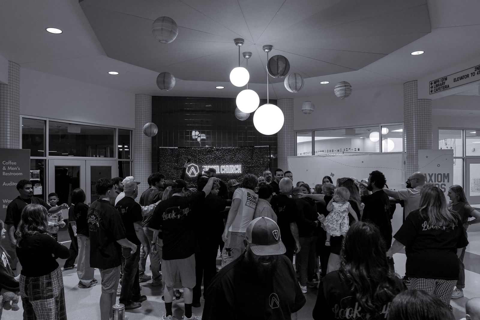 A crowd from Axiom huddled together in the lobby under the neon Axiom Church sign
