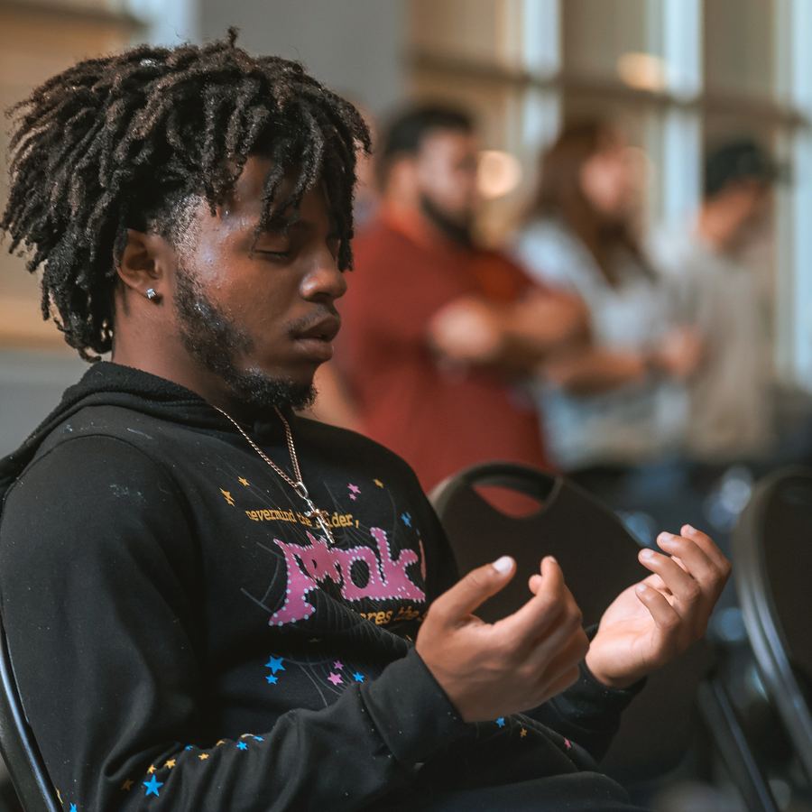 A young man sitting with his eyes closed and his hands open in front of him, praying