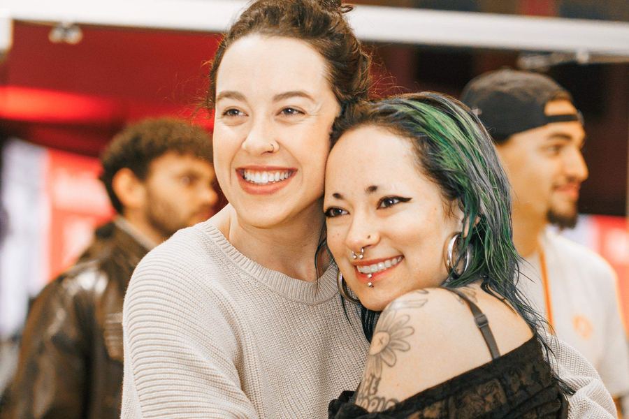 Two women hugging, one with tattoos and green hair, both smiling