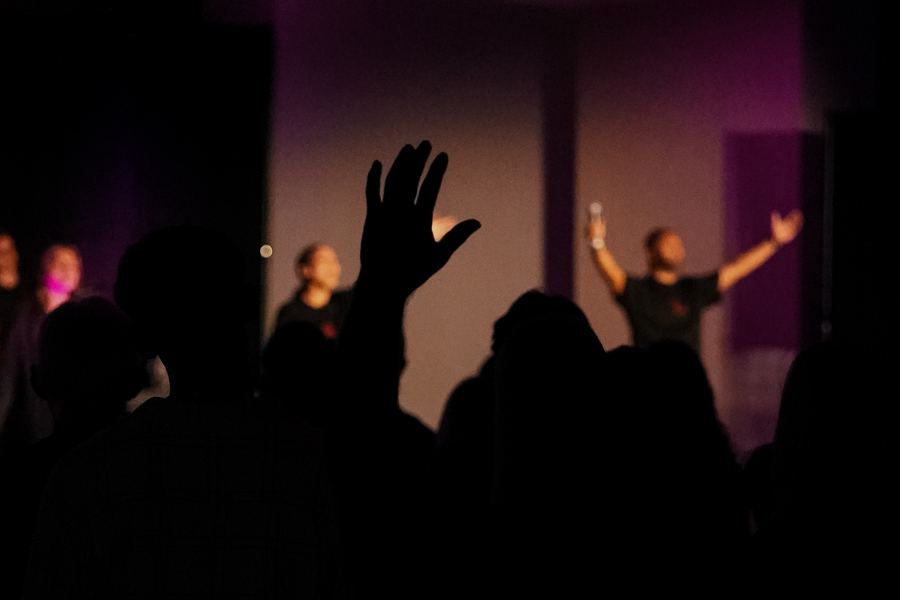 A raised hand in the crowd, with the worship team lit up on stage